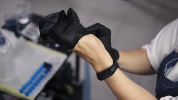 女性纹身大师戴上黑色橡胶手套的高角镜头，准备为她的客户纹身。 穿着黑色运动手表。 慢动作 — 图库视频影像