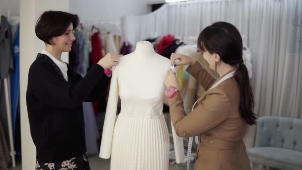 Alfaiates profissionais femininos, designers que trabalham com novo modelo alfaiataria vestido branco no manequim em estúdio, atelier. Fixação de mangas e fixá-los a partir dos lados. Moda e conceito de alfaiataria. Devagar. — Vídeo de Stock