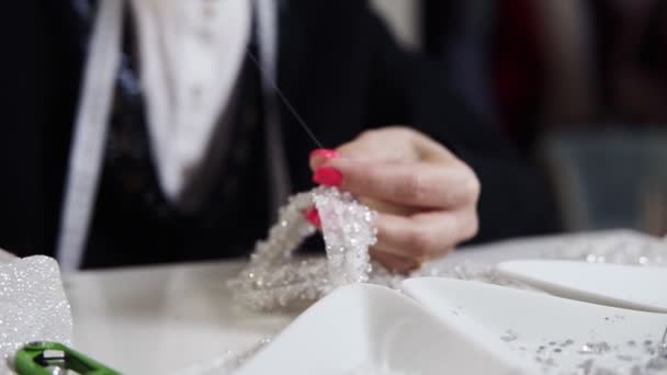 Close-up of female hands with pink manicure holding needle and thread and decorating exclusive wedding dress with decorative stones. Sewing elegant wedding dress. Hand made — Stock Video