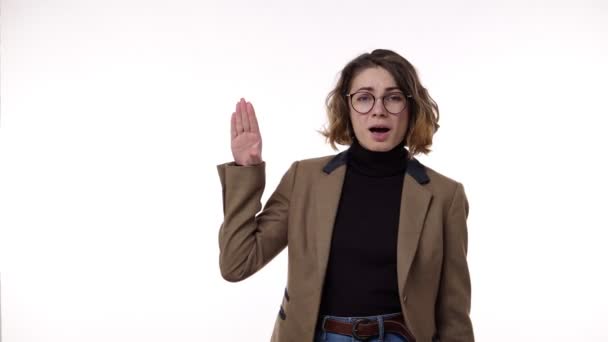 Annoyed pretty woman standing in front the camera isolated on a white background and showing blahblah gesture, gossips. Irritated, emotional. Wearing brown, retro jacket, jeans and stylish glasses — Stock Video