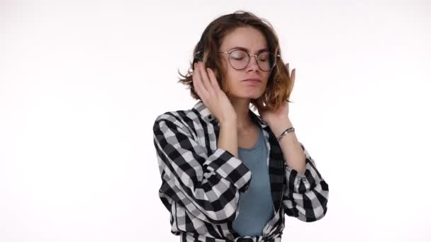 Jolie jeune fille en chemise à carreaux dansant et chantant avec de la musique de gros écouteurs et se sentent bien concept isolé sur fond de studio blanc — Video