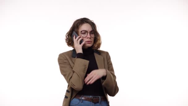 Mujer europea confusa sosteniendo el teléfono celular que tiene problemas con la persona que llama, chica enojada frustrada recibió malas noticias en el teléfono inteligente molesto por el spam o la llamada no deseada sobre fondo blanco — Vídeo de stock