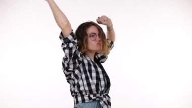 Young woman in plaid shirt listening to music using headphones standing over isolated white background very happy and excited doing dance with arms raised, emotionally moves. Slow motion