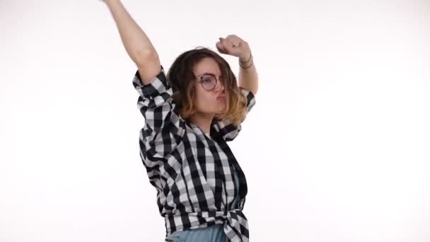Jovem mulher de camisa xadrez ouvindo música usando fones de ouvido em pé sobre fundo branco isolado muito feliz e animado fazendo dança com os braços levantados, emocionalmente se move. Movimento lento — Vídeo de Stock