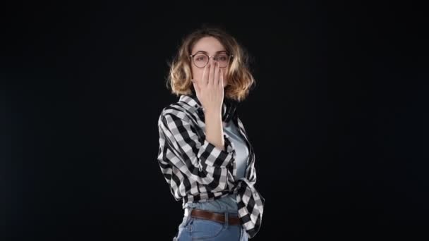 Atraktivní mladá Evropanka fouká rty, posílá spoustu vzduchových polibků izolovaných na černém pozadí ve studiu v neformálním oblečení a sluchátkách na krku. Lidé upřímné emoce, životní styl koncepce — Stock video