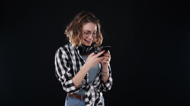 Ευρωπαϊκή κομψή νεαρή γυναίκα λαμβάνει καλά νέα, ενώ ανάγνωση από την οθόνη στο κινητό τηλέφωνο απομονώνονται σε μαύρο φόντο και πήρε σούπερ ενθουσιασμένος. Έννοια συναισθημάτων — Αρχείο Βίντεο