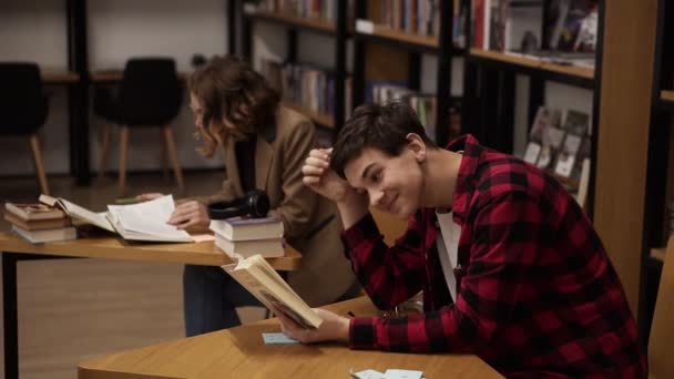 Estudiante europeo concentrado preparándose para el examen y leyendo libros mientras está sentado en la mesa de la biblioteca universitaria con sus compañeros de clase estudiando libros — Vídeos de Stock