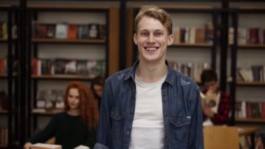 Close up portrait attractive young man laughing enjoying successful lifestyle achievement cheerful caucasian male in library bookshelf and classmates on background college education