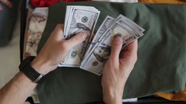 Unrecognizable man hands with pile of money, US dollars notes - counting under the suitcase with clothes. Counting money for holidays, vacation. Top view, close up. Wearing black hand watches — 비디오