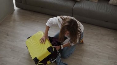 Seyahat çantası hazırlanıyor. Genç bir kadın toplanıyor ve umutsuzca valizini kapatmaya çalışıyor ve oturma odasında yerde otururken fermuarını kapatıyor.