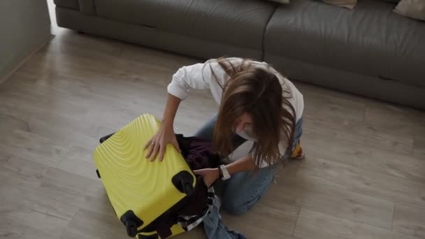 Zak klaarmaken voor de reis. Jonge vrouw inpakken en wanhopig proberen om volledige koffer te sluiten en sluit een rits op het terwijl zitten op de vloer in de woonkamer — Stockvideo