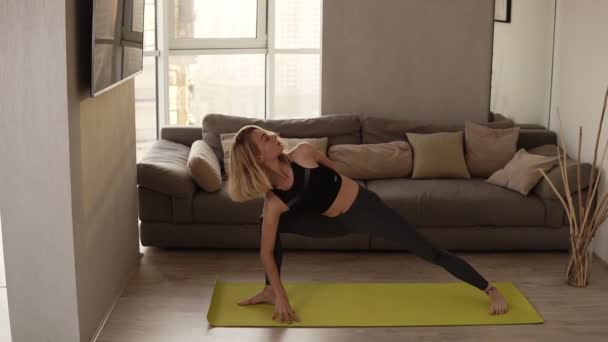 Das wunderschöne Mädchen in Sportkleidung übt zu Hause Yoga, während es in einem Asanas-Komplex trainiert. Jugend- und Sportkonzept. Zeitlupe — Stockvideo