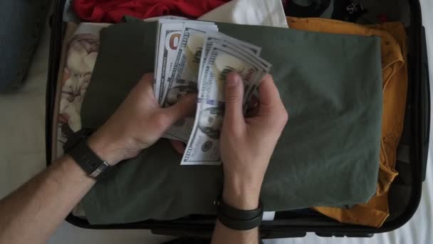 Uomo irriconoscibile mani con mucchio di soldi, banconote in dollari USA contando sotto la valigia con i vestiti. Contando i soldi per le vacanze, le vacanze. Vista dall'alto, da vicino — Video Stock