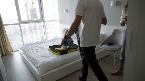 Family packing for holiday. Caucasian man, woman and child in bedroom. Trying to pack their clothes while little kid is sitting in the small yellow suitcase. Slow motion — Stock Video