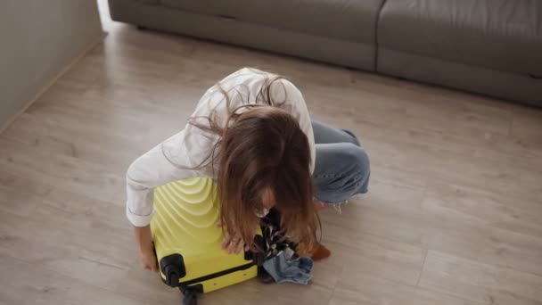 Preparing bag for travel. Young woman packing and desperatly trying to close full suitcase, sits on it and closes a zipper being on the floor in the living room. High angle view — 비디오