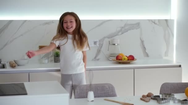 Menina bonita feliz dançando na cozinha moderna se divertindo fazendo movimentos de dança engraçados. Cabelo comprido, menina sorridente desfrutando fim de semana em casa. Movimento lento — Vídeo de Stock