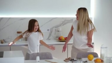 Modern, beyaz mutfakta mutlu bir aile. Beyaz giysili anne ve kızı rahatça dans ediyorlar. Annem mutfakta kızıyla dans ediyor. Yavaş çekim