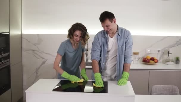 Pareja con cuatro manos que limpian el panel de cocina en la cocina. Hombre y mujer jóvenes limpiando la superficie perfecta de la cocina de cerámica negra con guantes y fregona. Divirtiéndose. Movimiento lento — Vídeos de Stock