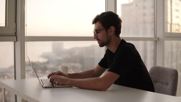 Joyful man using laptop computer at remote workplace in slow motion. Freelancer working on computer at home. Good looking man actively typing on laptop, chatting with friends at big house with — Stock Video