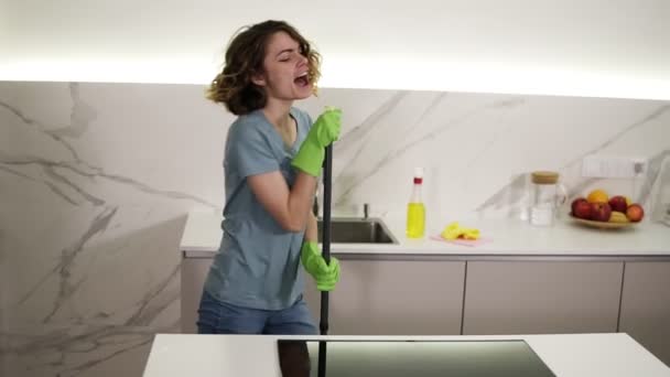 Ευτυχισμένη νεαρή γυναίκα χαριτωμένο νοικοκυρά πλένει το πάτωμα με σφουγγαρίστρα και χορό και το τραγούδι στο σπίτι στην κουζίνα απολαμβάνοντας οικιακές εργασίες. Άνθρωποι, μοντέρνος τρόπος ζωής και νεότητα — Αρχείο Βίντεο