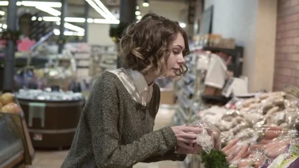 Красивая молодая красивая кудрявая женщина покупает еду в супермаркете. Девушка выбирает овощи-лук и свежую морковь в магазине. Концепция покупок. Размытый фон — стоковое видео