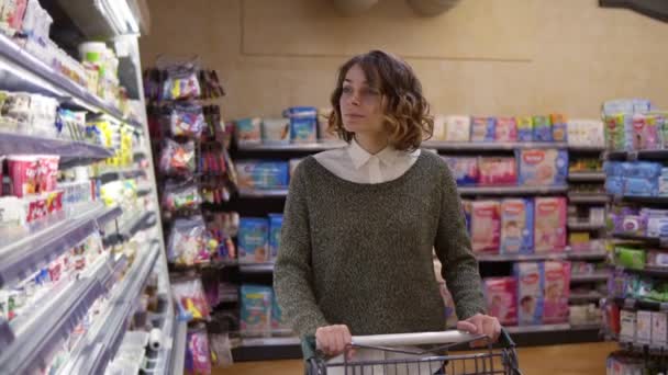 Comida, concepto de salud - Mujer en un supermercado de pie frente a los estantes del congelador y elegir la compra de una botella de jogurt, tomando uno y lo puso en el carro. Movimiento lento — Vídeos de Stock