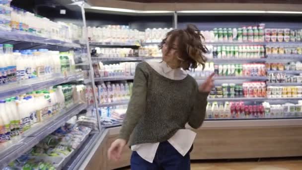 Mujer joven bailando por los pasillos de la tienda de comestibles. Mujer excitada divirtiéndose, bailando supermercado. Movimiento lento — Vídeo de stock