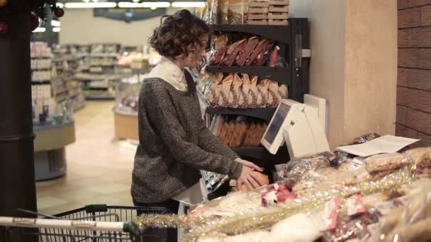 Een meisje weegt pomelo op een elektronische weegschaal in een supermarkt en plakt een sticker met een prijs. Pomelo in een rasterpakket. Zijaanzicht. Langzame beweging — Stockvideo