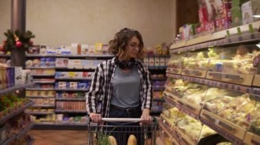 Boynunda kulaklığı olan çekici kız müşterisi fırın bölümünde ekmek alıyor, dükkana bakıyor ve alışveriş arabası koyuyor. Sağlıklı yaşam tarzı ve süpermarket kavramı