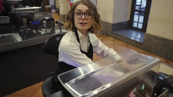 Vendedora caucásica alegre en camisa blanca y producto de escaneo delantal negro, frutas en el mostrador de pago en el supermercado brillante y ponerlo en una bolsa de papel marrón, tomar un CE del cliente y deslizar — Vídeo de stock