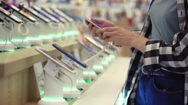 Tanımlanamayan kadınların belden aşısı bir elektronik mağazasından akıllı telefon seçiyor. Tezgahtan akıllı telefonu alıp kullanmaya çalışıyor. Yan görünüm