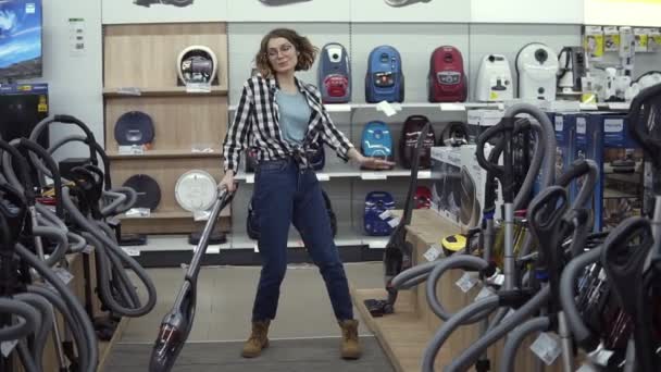 Funny caucasian woman in casual standing in home appliance store - dancing, having fun with hand helded vacuum cleaner, funky dances — Stock Video