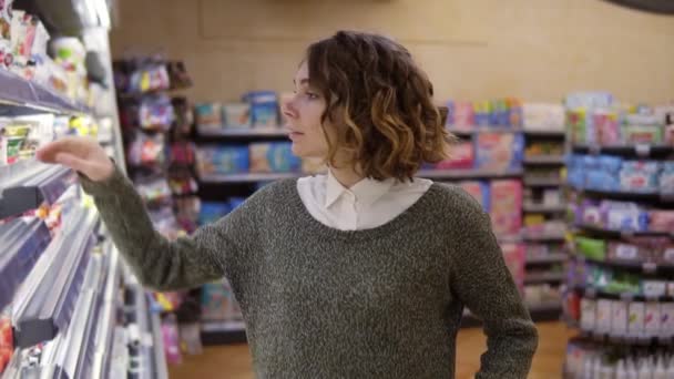 Comida, concepto de salud - Mujer en un supermercado de pie frente a los estantes del congelador y elegir la compra de una botella de jogurt, tomando uno y lo puso en el carro. En cámara lenta. De cerca. — Vídeos de Stock