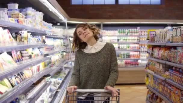 Porträt einer glücklichen, entspannten Frau mit lockigem Haar, die mit einem Einkaufswagen einkaufen ging - reihenweise spazieren ging und fröhlich in entspannter Stimmung tanzte. Zeitlupe — Stockvideo