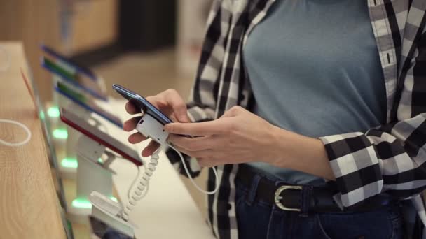 Cintura tiro de mãos mulheres irreconhecíveis escolhe um smartphone em uma loja de eletrônicos. Ela tira o telefone inteligente do balcão e tenta usá-lo. Fechar — Vídeo de Stock