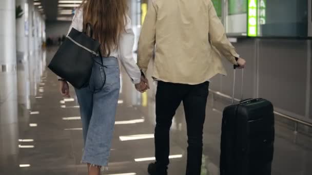 Rara vista de pareja caminando juntos en el aeropuerto yendo de vacaciones o de viaje. Viajen juntos. Lleva mochila y maletas. Atractiva joven mujer en jeans y hombre con maletas están listos para viajar — Vídeo de stock