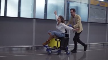 Havaalanındaki komik çift. Çekici genç kadın ve bavullu yakışıklı adam seyahat etmeye hazırlar. Kalkışı beklerken bagaj vagonunda eğleniyoruz. Uçan, gülümseyen bir kadın.