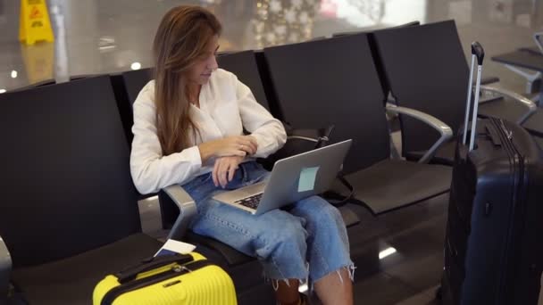 Довгошерста сучасна жінка сидить у вітальні і використовує ноутбук для роботи в аеропорту. Дівчинка-туристичний фрілансер працює і чекає на політ у залі очікування. Концепт подорожі, віддалена робота — стокове відео