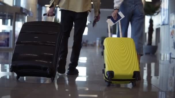 Un par de viajeros llevan su equipaje y pasaportes. Caminando sobre el salón de la terminal, vista trasera. La gente se está preparando para abordar y salir. Cierre de maletas enrollables. Movimiento lento — Vídeo de stock