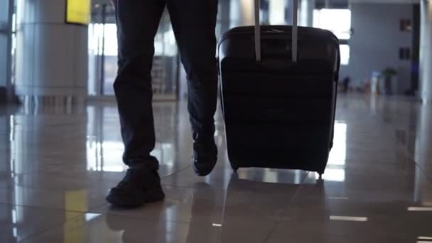 Primer plano, plano recortado de las piernas del hombre con el equipaje negro caminando a la terminal del aeropuerto. En cámara lenta. Vista frontal — Vídeos de Stock