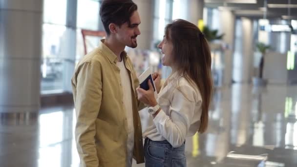 Emocionada, mujer mostrando pasaporte con sello de visa a su novio en el aeropuerto. Pareja feliz, hombre abrazando a su novia y están esperando el avión. Movimiento lento — Vídeo de stock