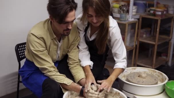 Romantiskt, ungt par som har roligt när de arbetar tillsammans i keramikverkstad. Sitter vid keramiker hjul, kvinna lekfullt markerar sina pojkvänner näsa med lera. Långsamma rörelser — Stockvideo