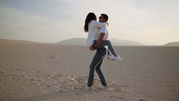 Escena perfecta de pareja joven en el desierto vacío. hombre sosteniendo a su mujer en brazos y darle la vuelta, divertirse emocionalmente, reír, sonreír al atardecer en el desierto loco en el amor, emociones y relación — Vídeo de stock