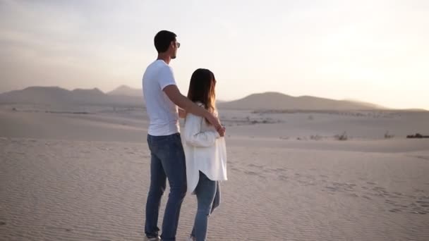 Fiatal pár áll és ölelkezik, férfi fogja a nő hátát a száraz, homokos sivatagban nézi a táj együtt gondolkodva — Stock videók