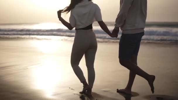Pihentető pár mezítláb sétál a strandon.Üres, békés parton töltik együtt az idejüket. Fiatal férfi és nő nászúton a trópusi tengerparton. Ritka kilátás — Stock videók