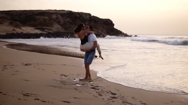 Pareja enamorada. Hombre con camisas girando alrededor de su encantadora mujer en la playa y besándose sensualmente. Vista completa de feliz joven descalzo hombre y mujer divirtiéndose juntos en la playa de arena — Vídeos de Stock