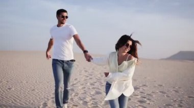 Güneşin altında koşan çiftler güneşli ve romantik ilişkilerde eğleniyorlar ve çölde mavi gökyüzü. Yazın romantizm içinde neşeli iki genç aşık. Günlük giysiler giyiyor.