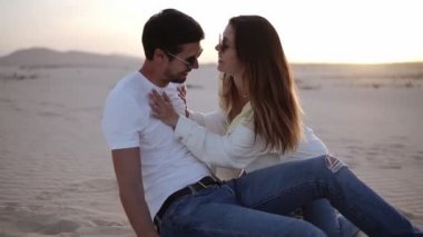 Genç adam ve kadın çölde kumların üzerinde eğleniyorlar. Güzel çift birbirine aşık, arka planda kumul manzarası. Hafif bir alacakaranlık. Romantik çift birlikte vakit geçiriyor. Yavaş çekim