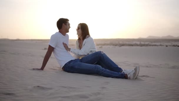 Joven hombre y mujer sentado en el desierto hermosa pareja chica y chico arena duna paisaje fondo. Atardecer suave. pareja romántica teniendo tiempo juntos — Vídeos de Stock