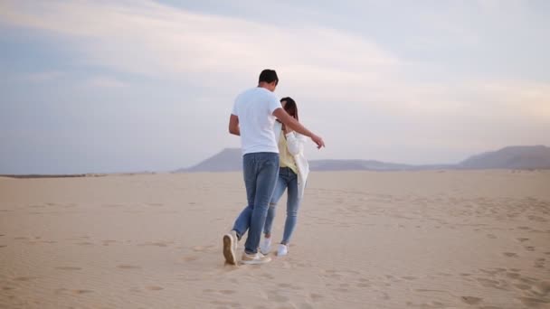 Bonita pareja alegre risueña con camisetas blancas casuales. Tipo moreno girando con su dama, cogido de la mano en movimientos. Bailando en la naturaleza en el desierto vacío. Longitud total. Movimiento lento — Vídeos de Stock